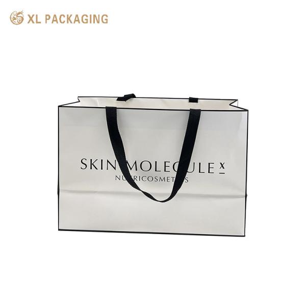 Custom branded luxury matte white coated art paper gift bag with wide black woven ribbon handle for cosmetic retail